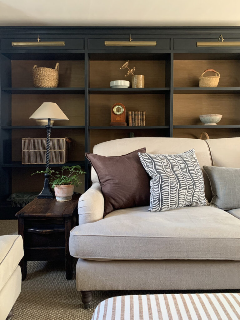 Neutral living room featuring the 60 30 10 rule with a beige sofa, black shelving, and warm decorative accents.