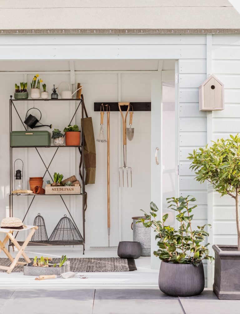 Tools neatly hung on the wall inside a white garden shed.